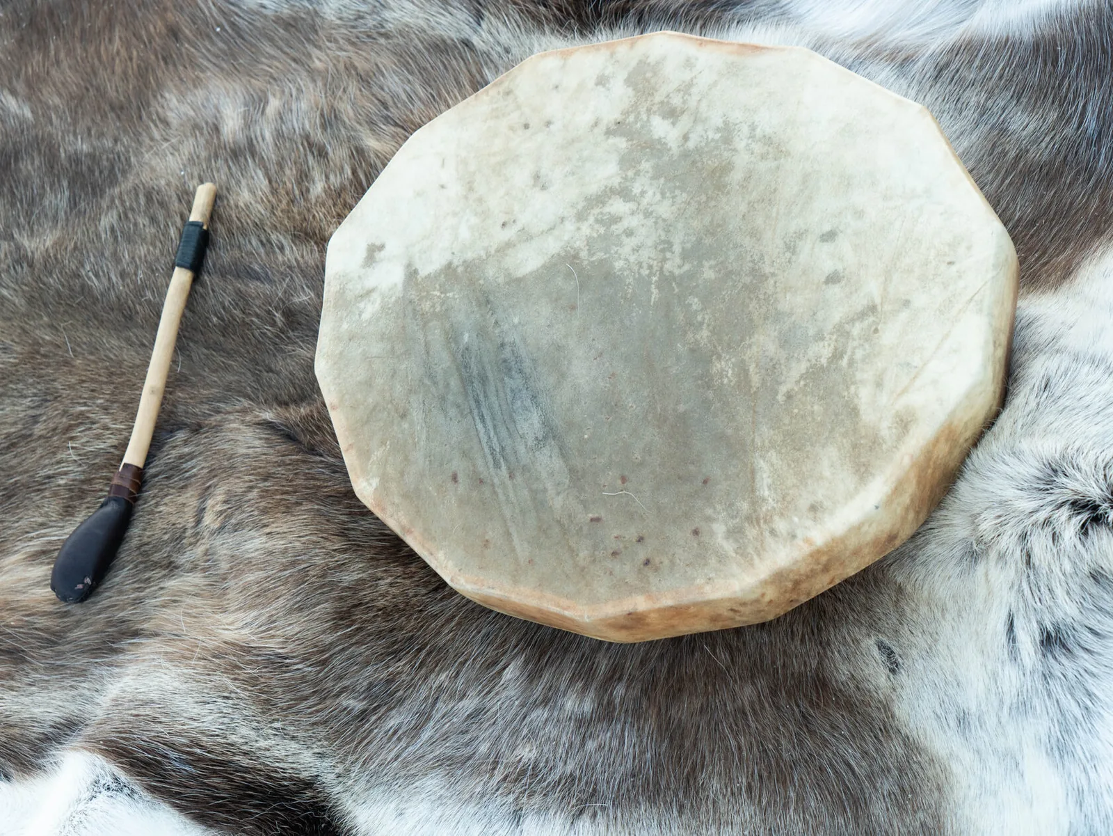 A traditional Sámi drum and beater resting on reindeer fur